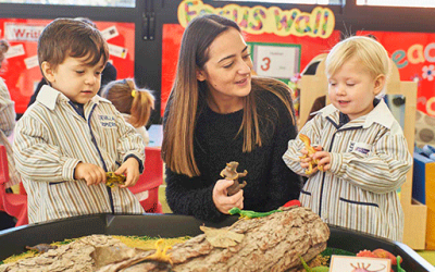 Two preschool children playing with dinosaurs with their teacher.