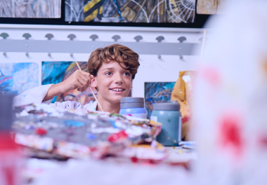 A primary student smiles while holding a paintbrush in art class.